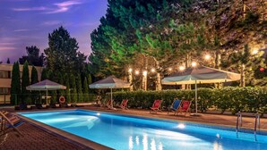 A swimming pool with lounge chairs and umbrellas, surrounded by trees and a brick walkway.