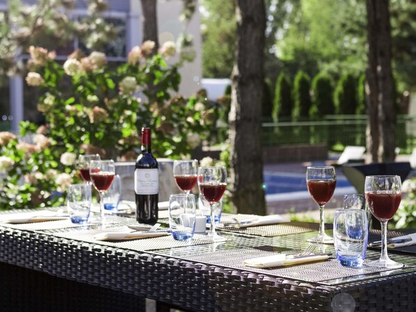 A table set outdoors with wine glasses and a bottle, surrounded by greenery. - Novotel Warszawa Airport (Warsaw)