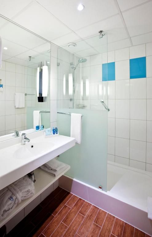 A modern bathroom with a large mirror, dual sinks, a shower, and a bathtub.