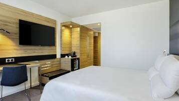 Una habitación de hotel moderna con una cama grande, un escritorio con una silla, un televisor de pantalla plana en la pared y un minibar.