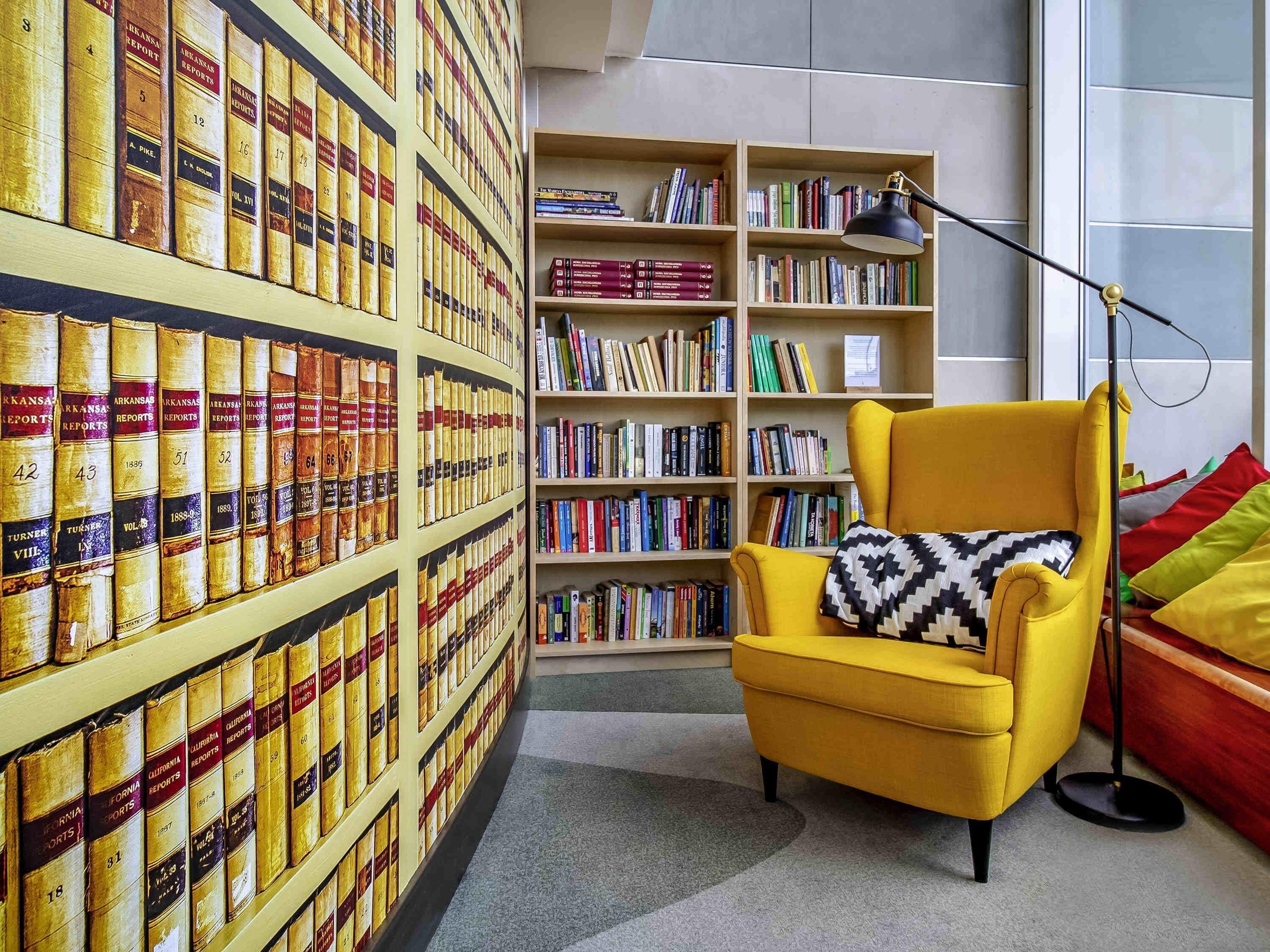 Een kamer met een boekenplank vol boeken, een gele fauteuil met een gestreept kussen, en een vloerlamp.