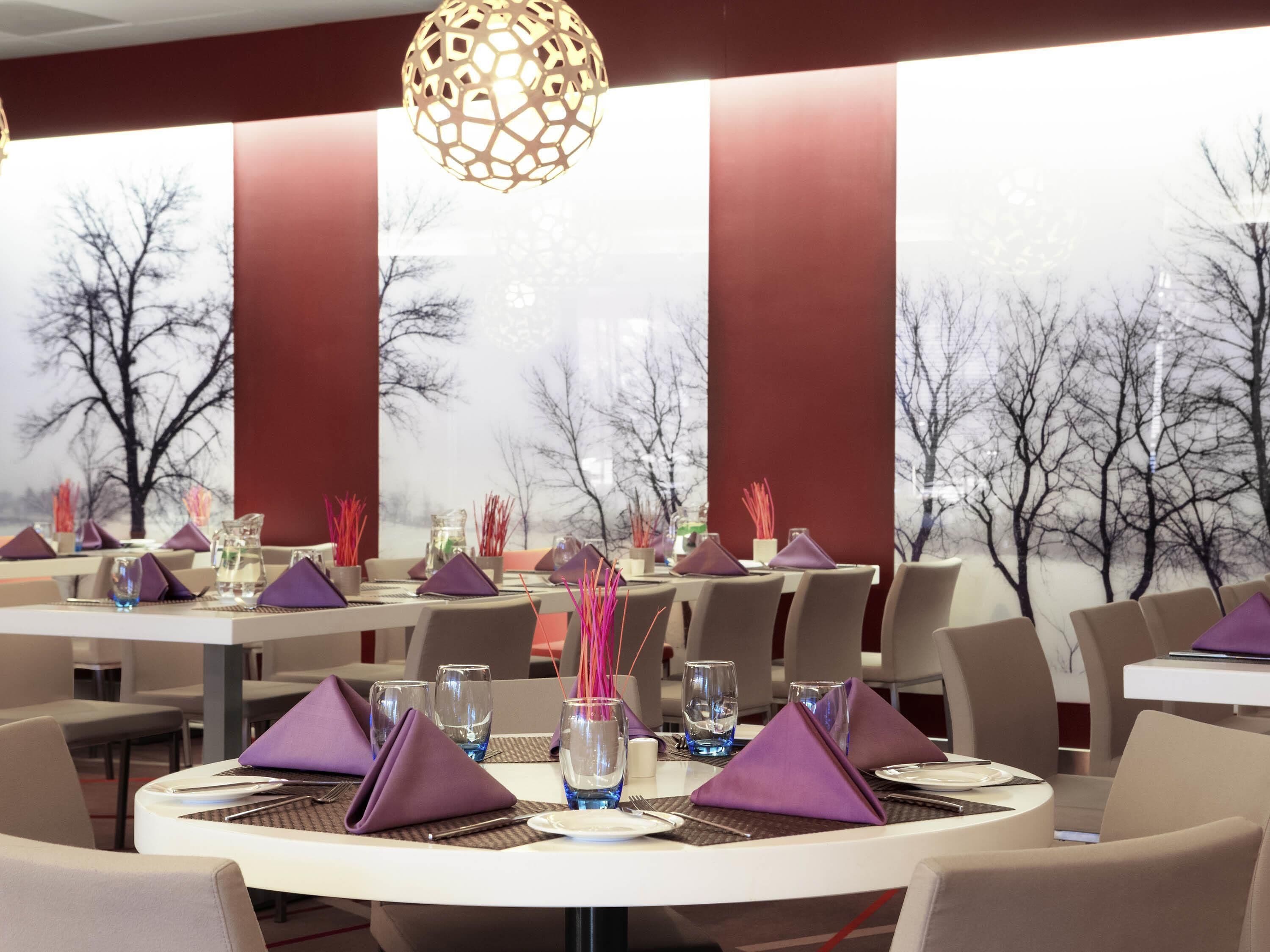 A restaurant with round tables, purple napkins, and a decorative hanging light fixture.