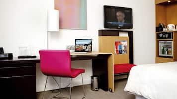A hotel room with a desk, a laptop, a television, a bed, and a minibar.