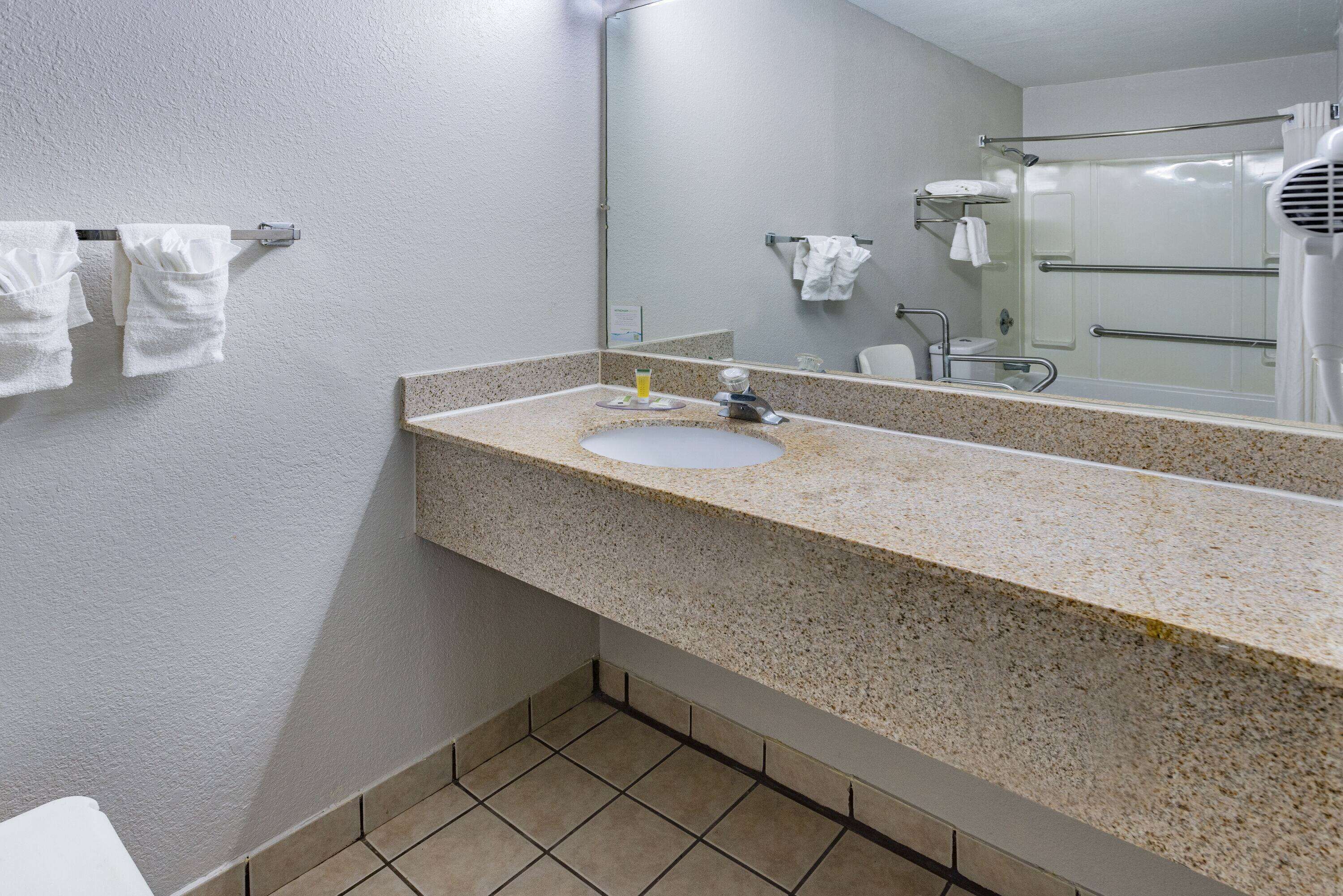 Een badkamer met een wastafel met granieten blad, een spiegel en een douche met een glazen deur.