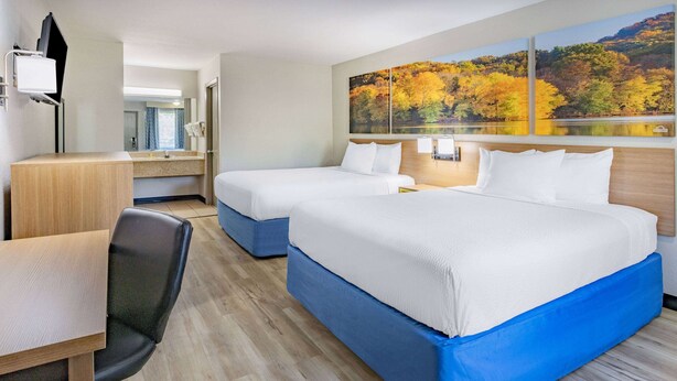 Habitación de hotel con dos camas, un escritorio, una silla y un amplio ventanal con una obra de arte que representa follaje otoñal.