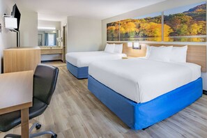 A hotel room with two beds, a desk, a chair, and a large window with autumn foliage artwork.