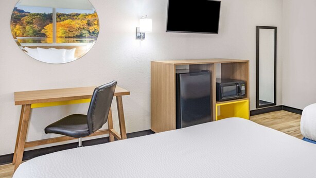 Habitación de hotel con una cama, un escritorio con silla, un televisor montado en la pared, un microondas y un refrigerador.