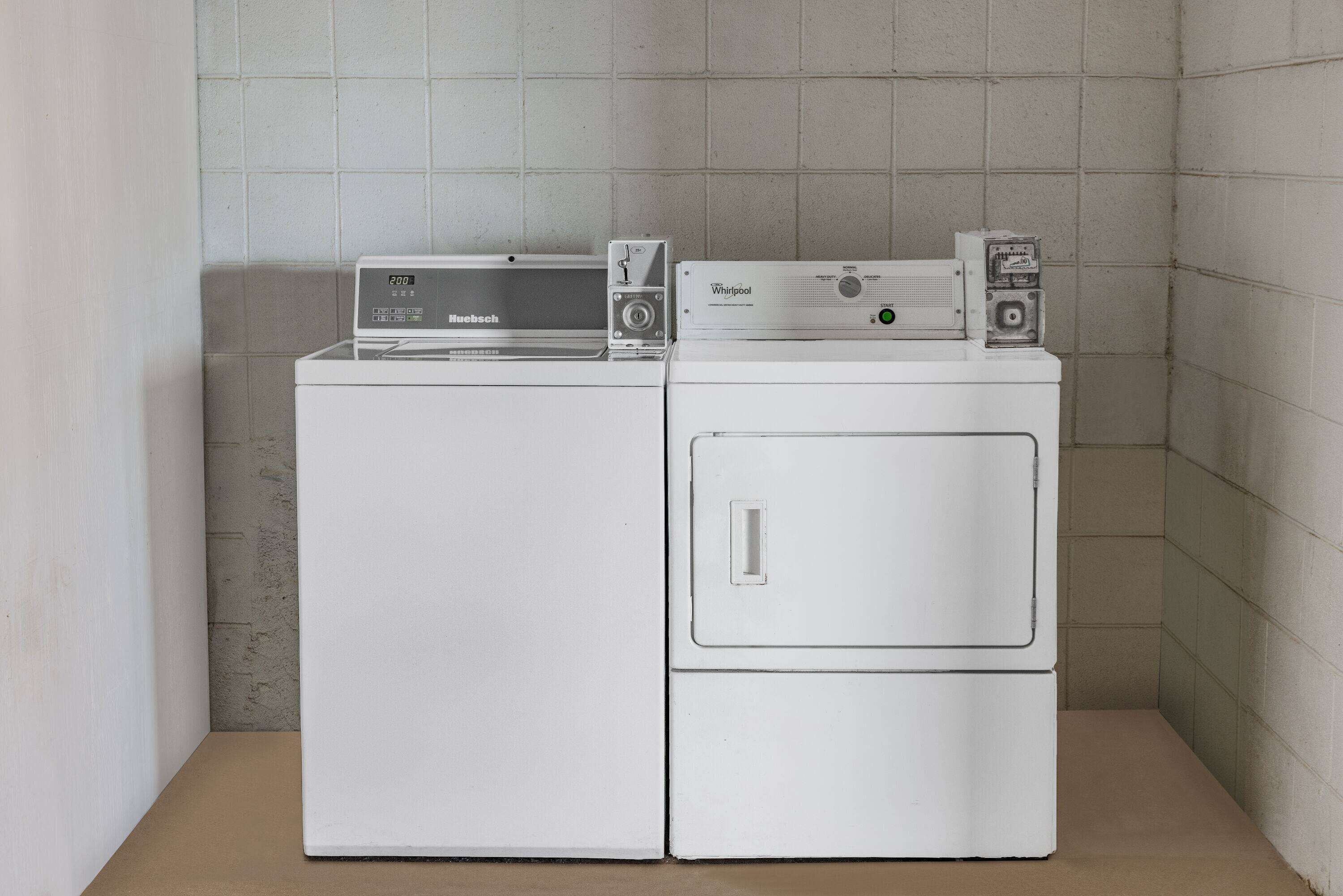 Een kleine wasruimte met een voorlader wasmachine en droger, een kleine verwarming en een bedieningspaneel.