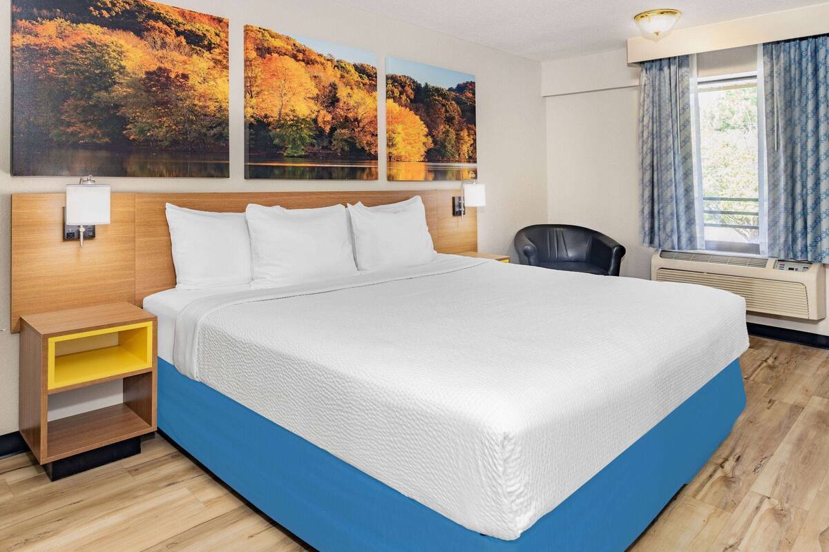 A hotel room with a large bed, a nightstand, a chair, and a window with curtains.