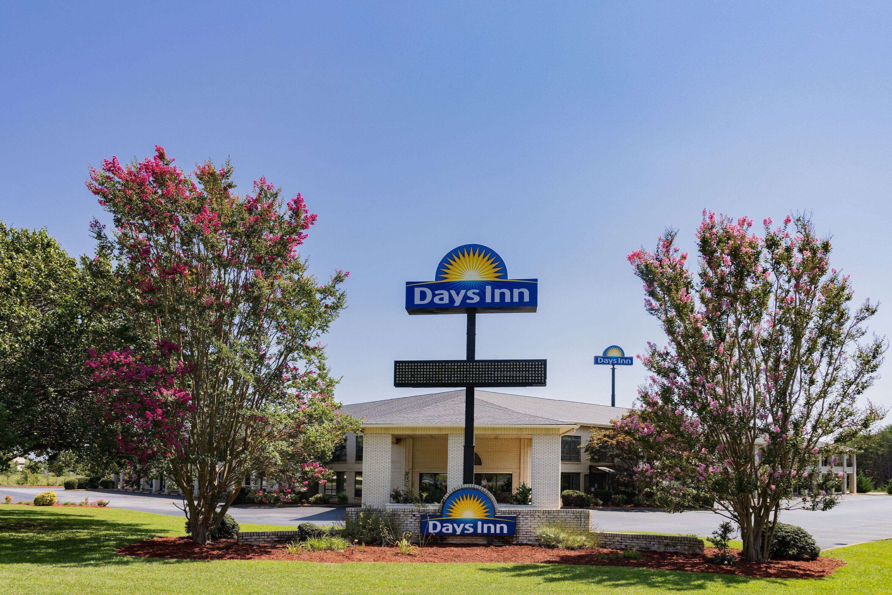 A Days Inn hotel with a clear sign, surrounded by flowering trees and a well-maintained lawn.