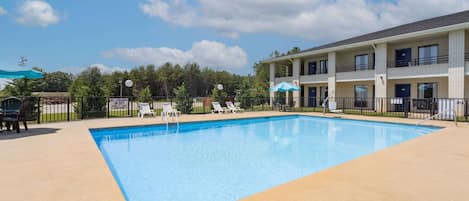 Una piscina con sillones de descanso y un edificio de varios pisos al fondo.