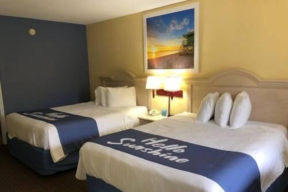 A hotel room with two beds, a nightstand, a lamp, and a painting on the wall.