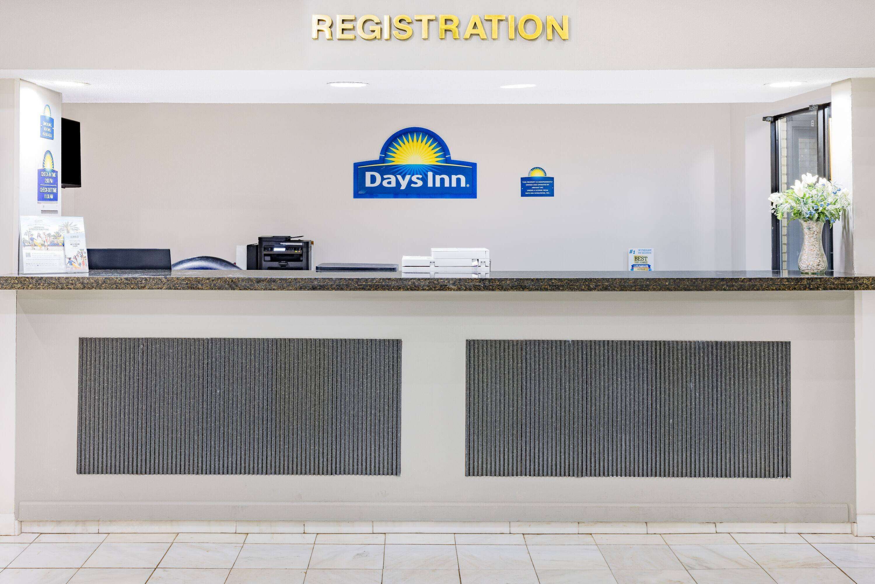 A reception desk with a 'Registration' sign, a Days Inn logo, and a vase with flowers.