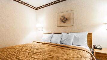 Una cama bien hecha con cubrecama acolchada, una lámpara de noche y una obra de arte enmarcada en la pared.