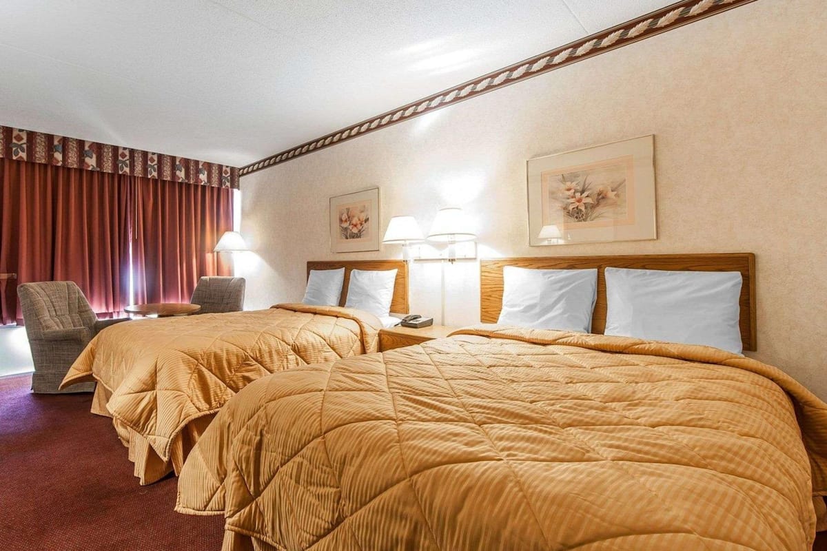 A hotel room with two beds, a chair, a lamp, and a framed picture on the wall.