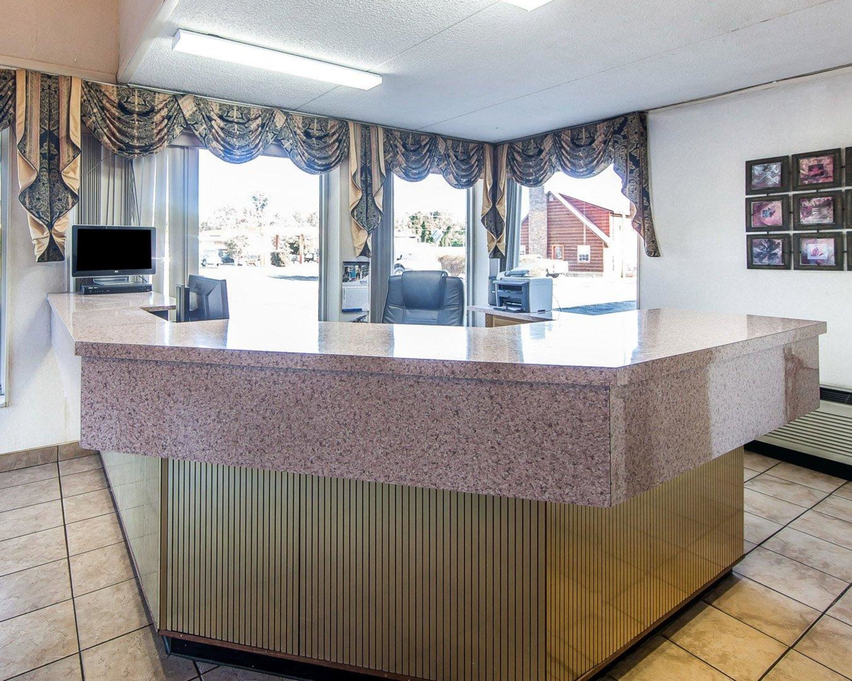 A reception desk with a granite top, a flat-screen TV, and a computer monitor. There are chairs and a small table in front of the desk.