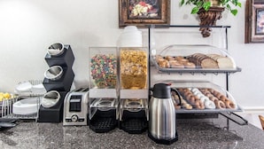 A breakfast buffet with cereal, pastries, and a coffee maker.
