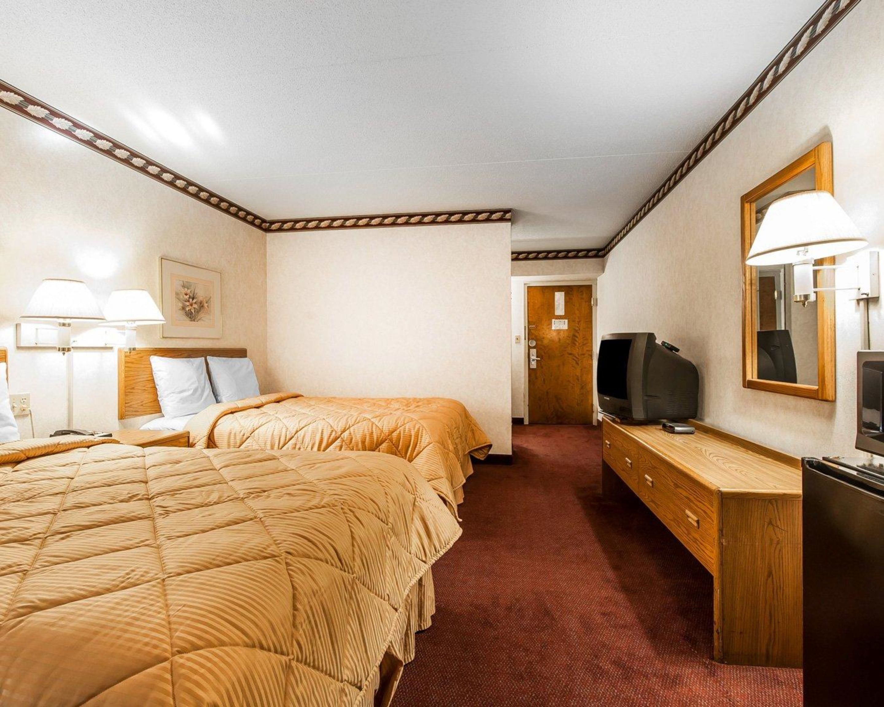 A hotel room with two beds, a television, a dresser, and a mirror.