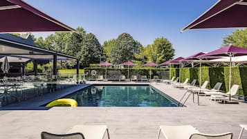 Une piscine entourée d’une haie et d’arbres, avec des chaises longues et des parasols.