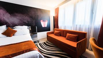 A hotel room with a bed, a sofa, a TV, and a large window with curtains.