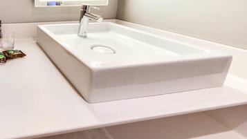 A white bathroom sink with a modern faucet, a mirror above it, and a small glass and a packet of toiletries on the counter.