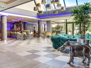 Un vestíbulo de hotel con piso de tablones, zona de bar, asientos y una gran estatua de toro.