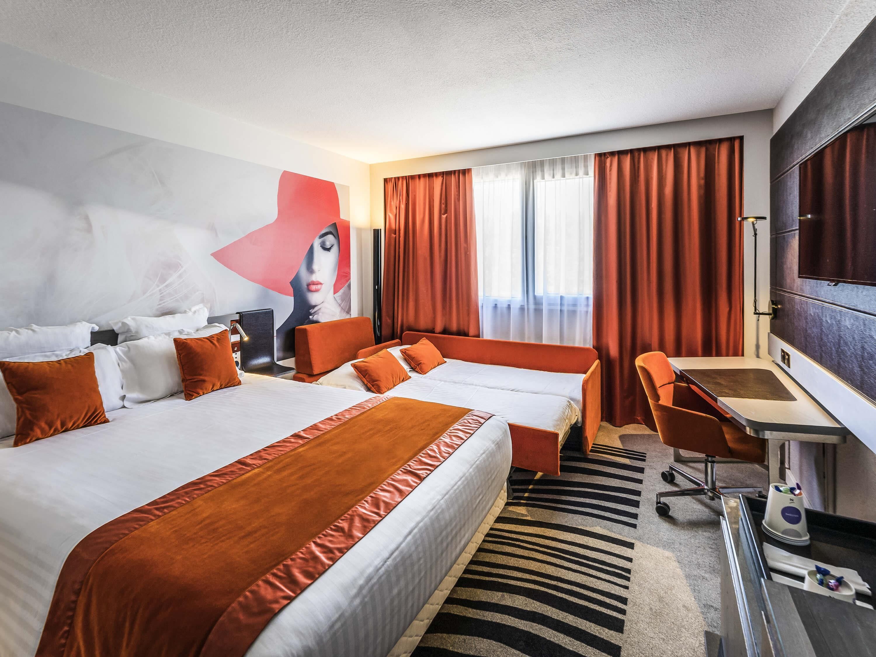 A hotel room with a large bed, a desk, a chair, a TV, and a painting on the wall.