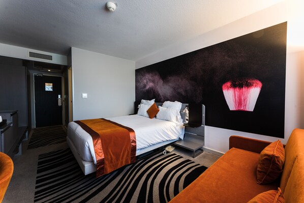 Una habitación de hotel con una cama, un sofá, un mural grande en la pared y un escritorio.