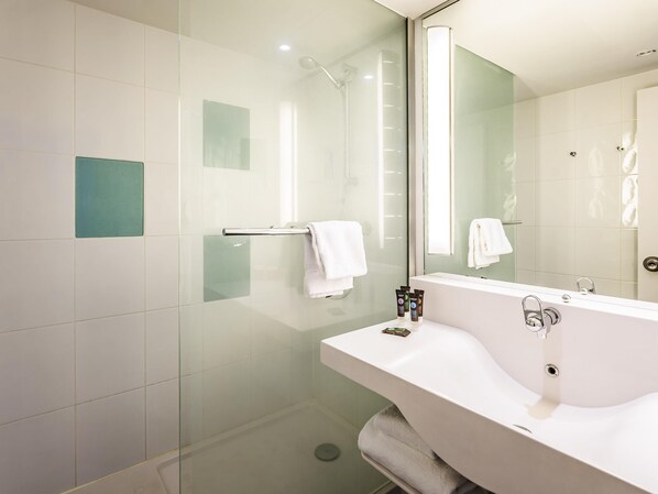 Un baño moderno con cabina de ducha de vidrio, un lavabo blanco y un espejo grande, además de un perchero para toallas.