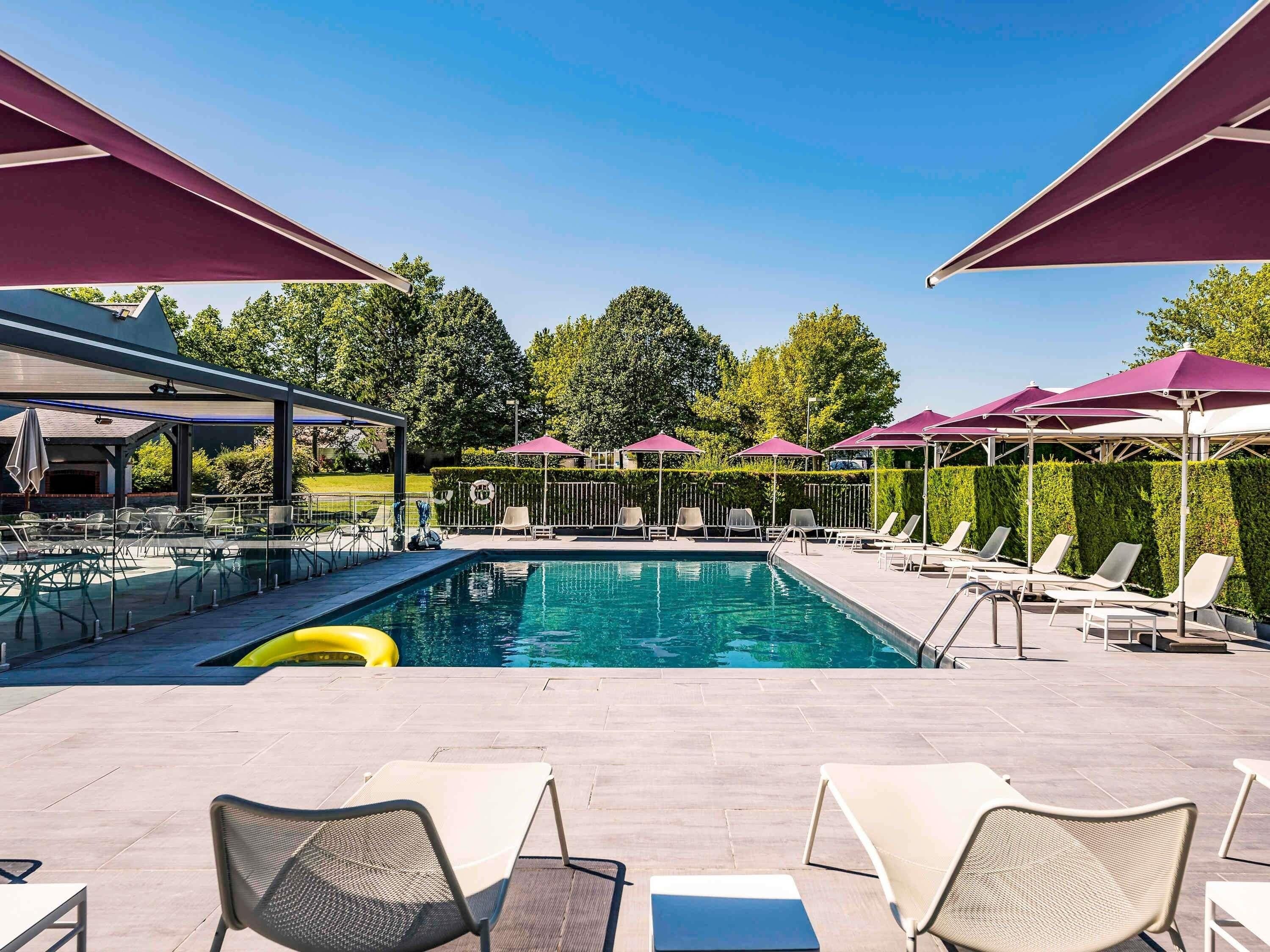 Une piscine entourée d’une haie et d’arbres, avec des chaises longues et des parasols.