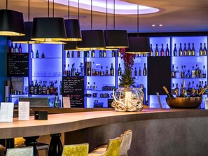 A bar area with multiple hanging lamps, a variety of bottles on shelves, and a decorative vase with flowers.