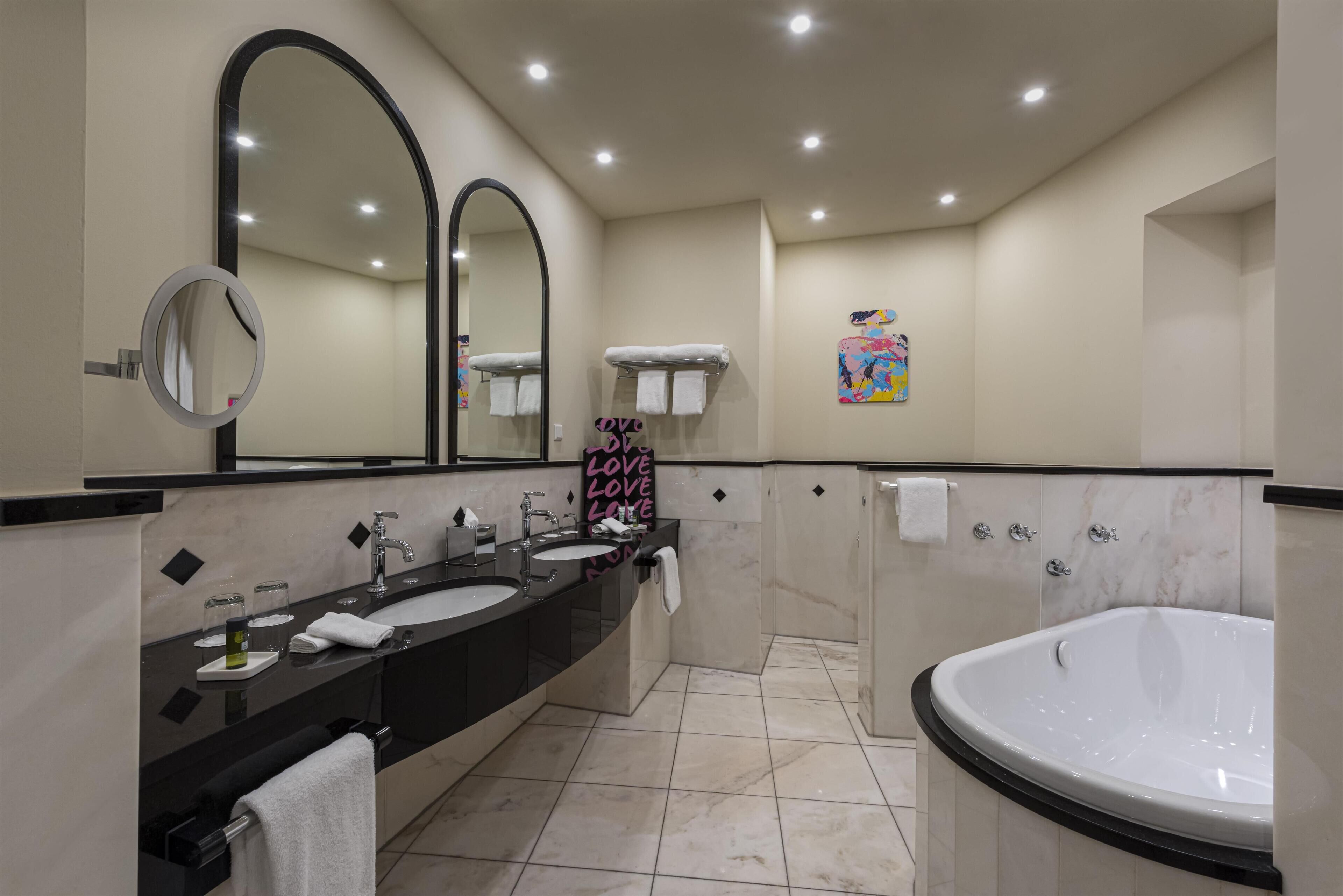 A modern bathroom with two sinks, a large mirror, a bathtub, and a towel rack.