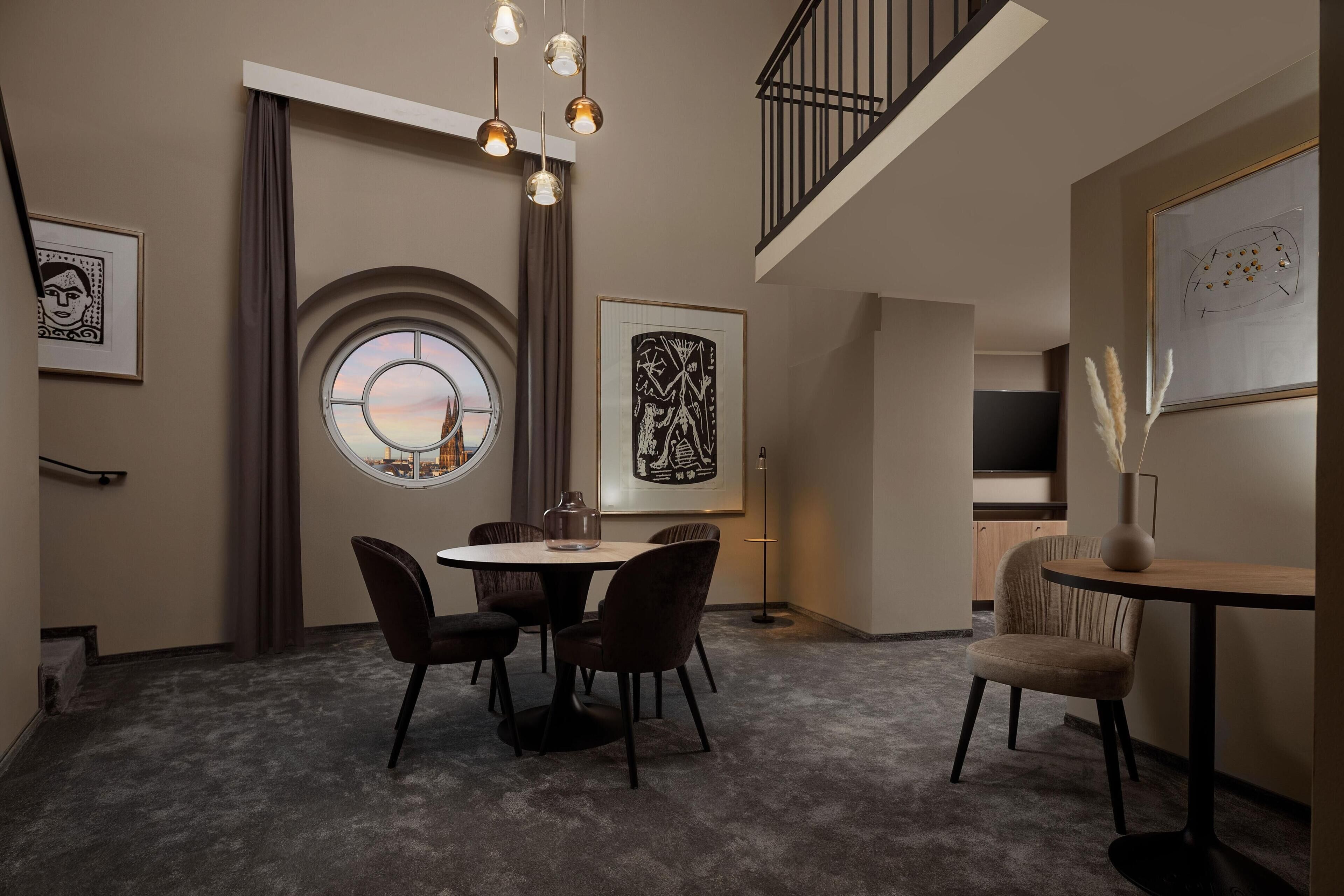 Een eetgedeelte met een ronde tafel, vier stoelen, een vaas en kunstwerken aan de muur.