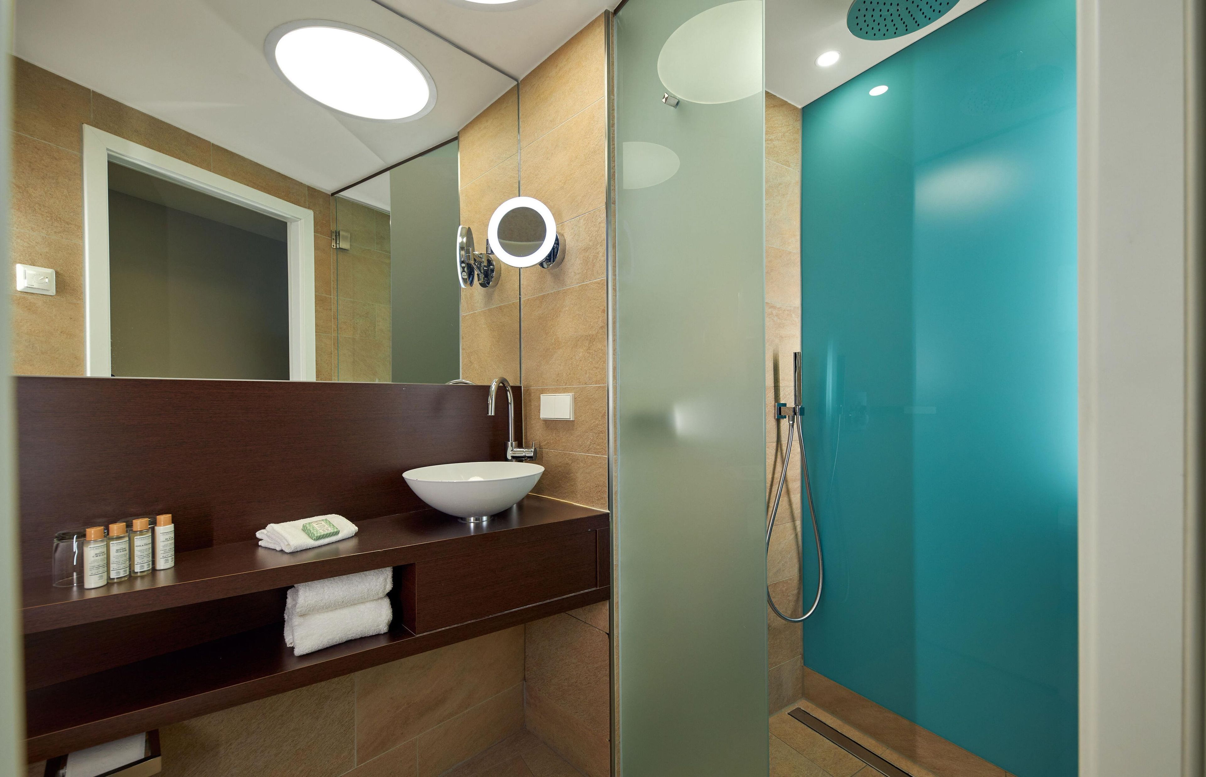 A modern bathroom with a large mirror, a white vessel sink, and a glass-enclosed shower.