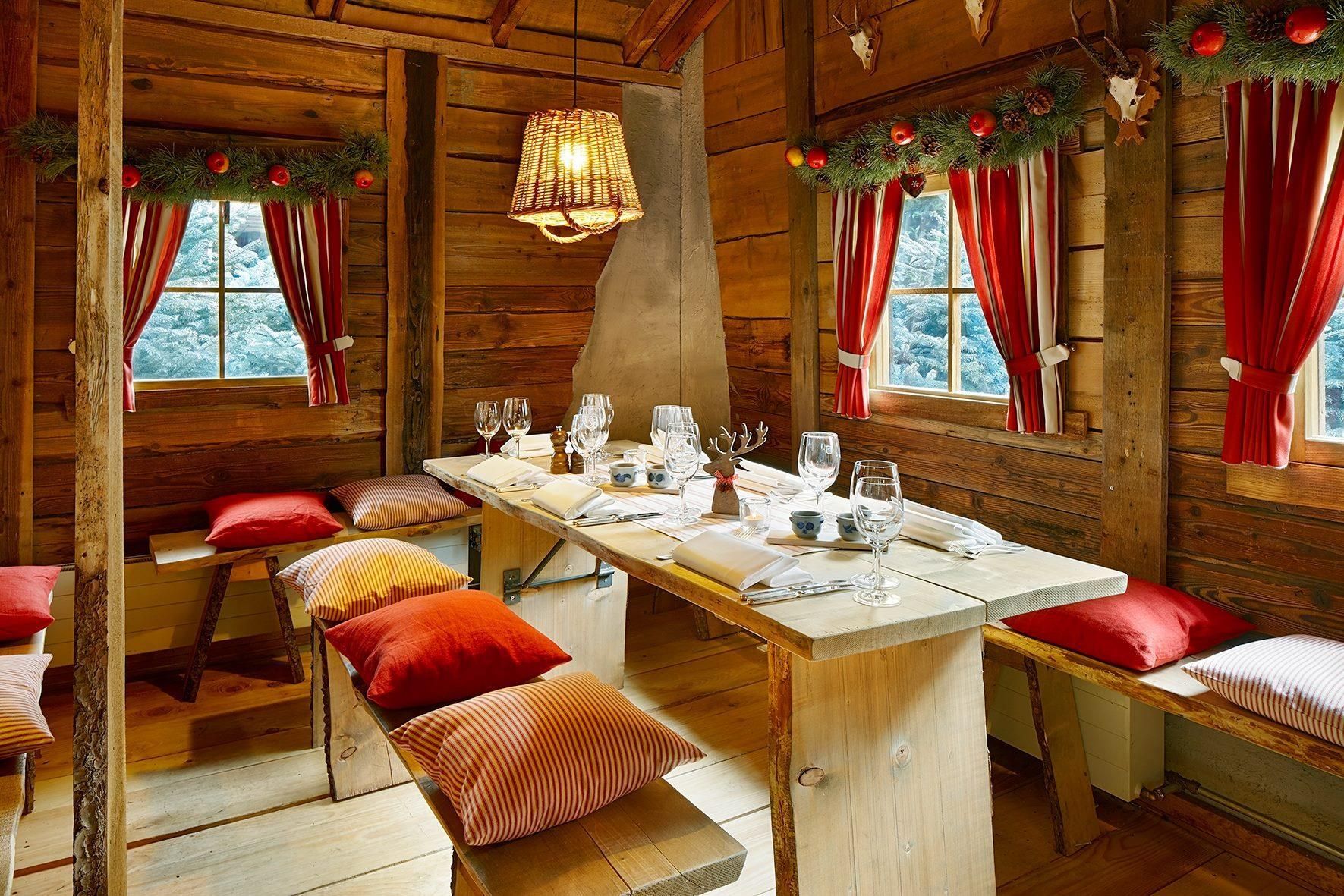 A wooden cabin with a dining table set for six, benches, and a fireplace.