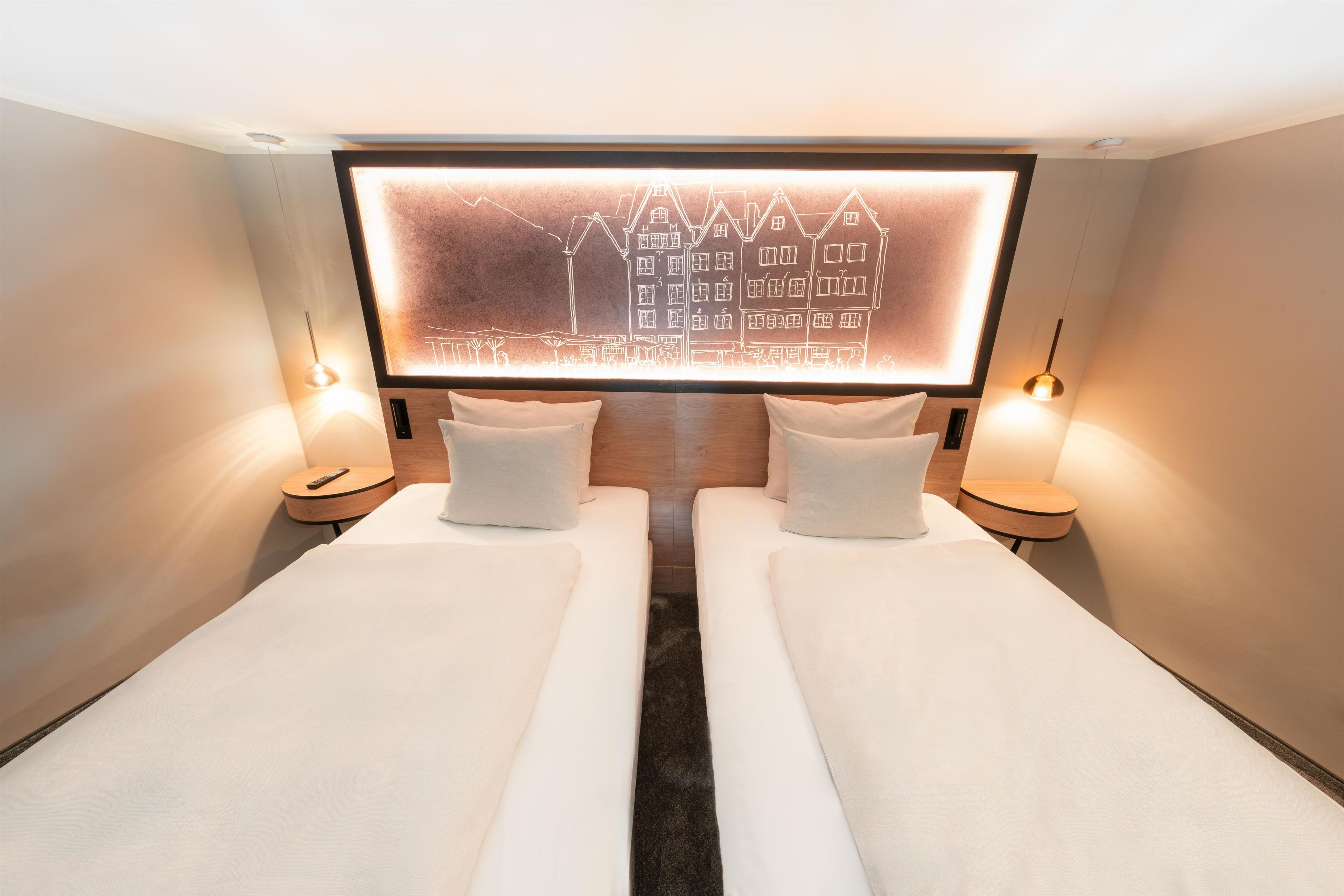 Ein Hotelzimmer mit zwei Einzelbetten, einer großen beleuchteten Wandkunst und Nachttischlampen.