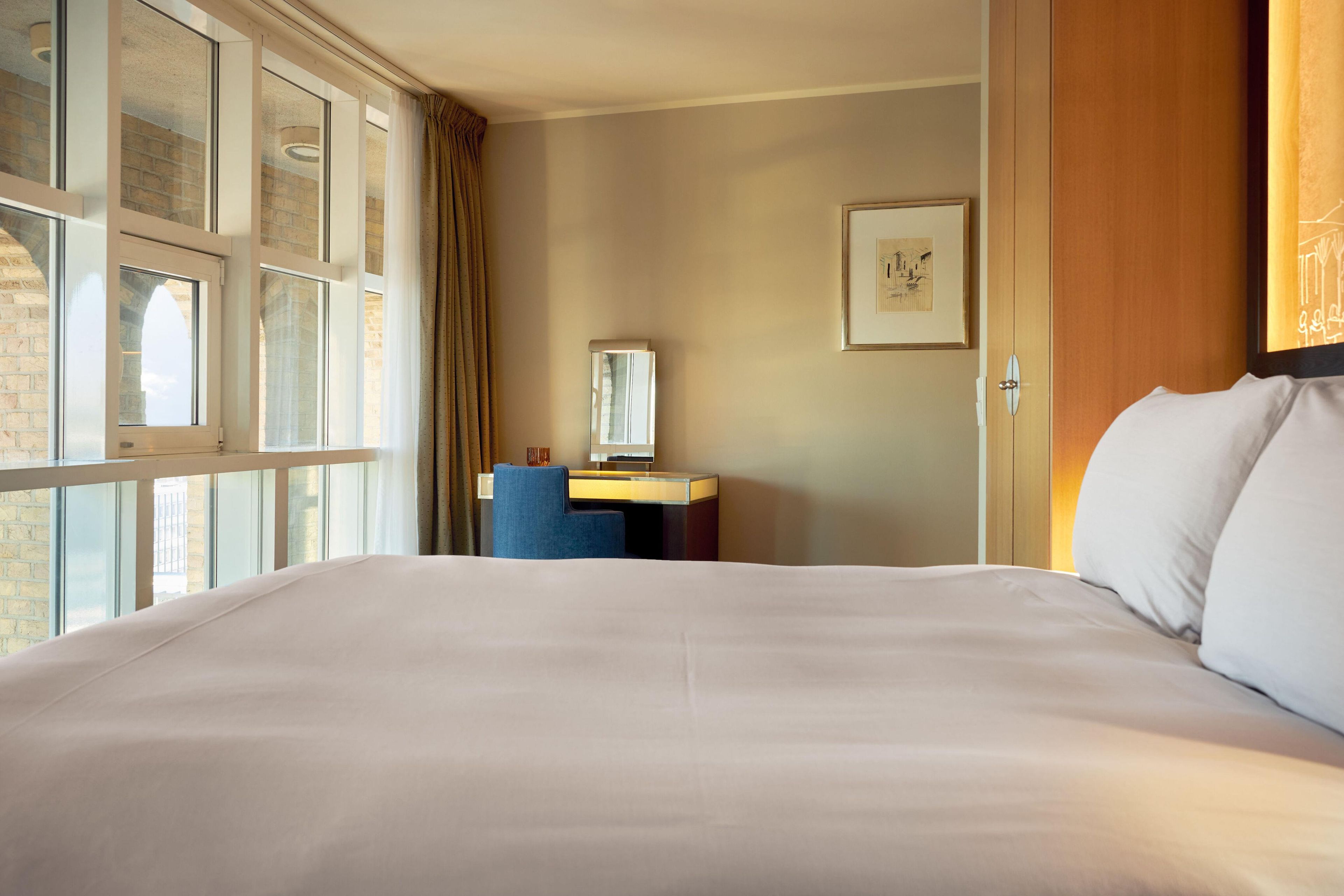 A hotel room with a large bed, a desk, a chair, and a window with curtains.