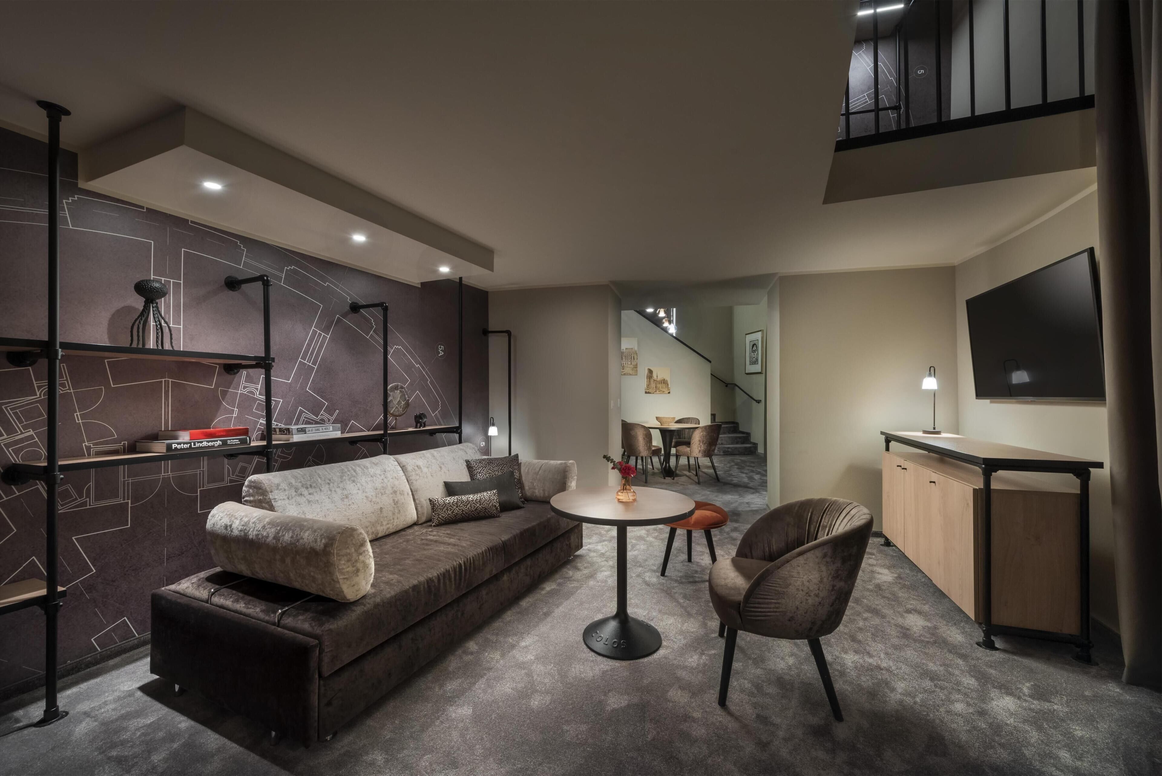 A modern living room with a sofa, a round table, a chair, a bookshelf, and a staircase leading to an upper level.