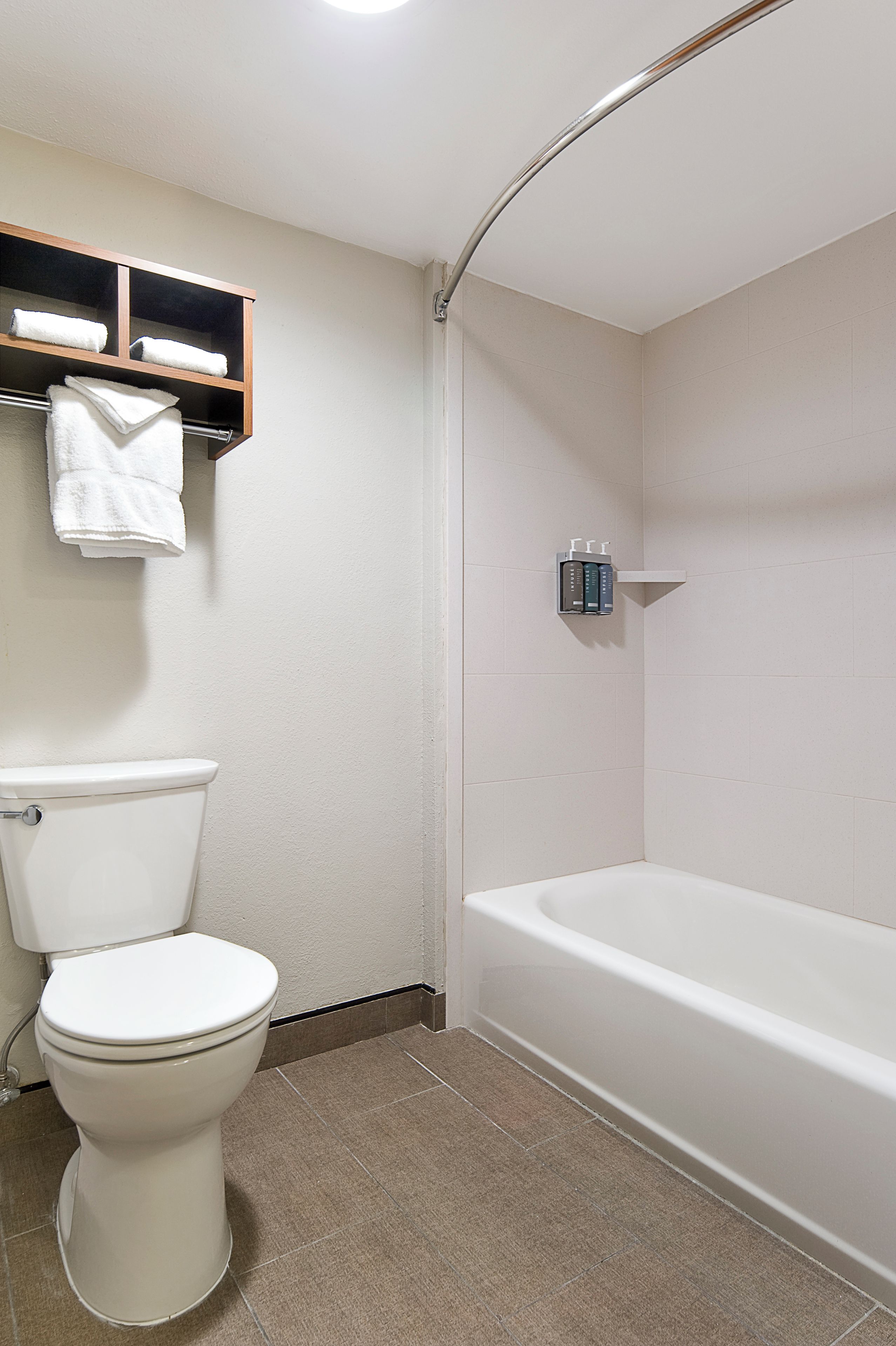 A bathroom with a toilet, a bathtub, a shelf with towels, and a soap dispenser.