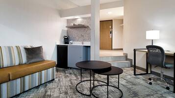 Habitación de hotel con sofá, una mesita redonda, escritorio con silla, kitchenette y baño a la vista.