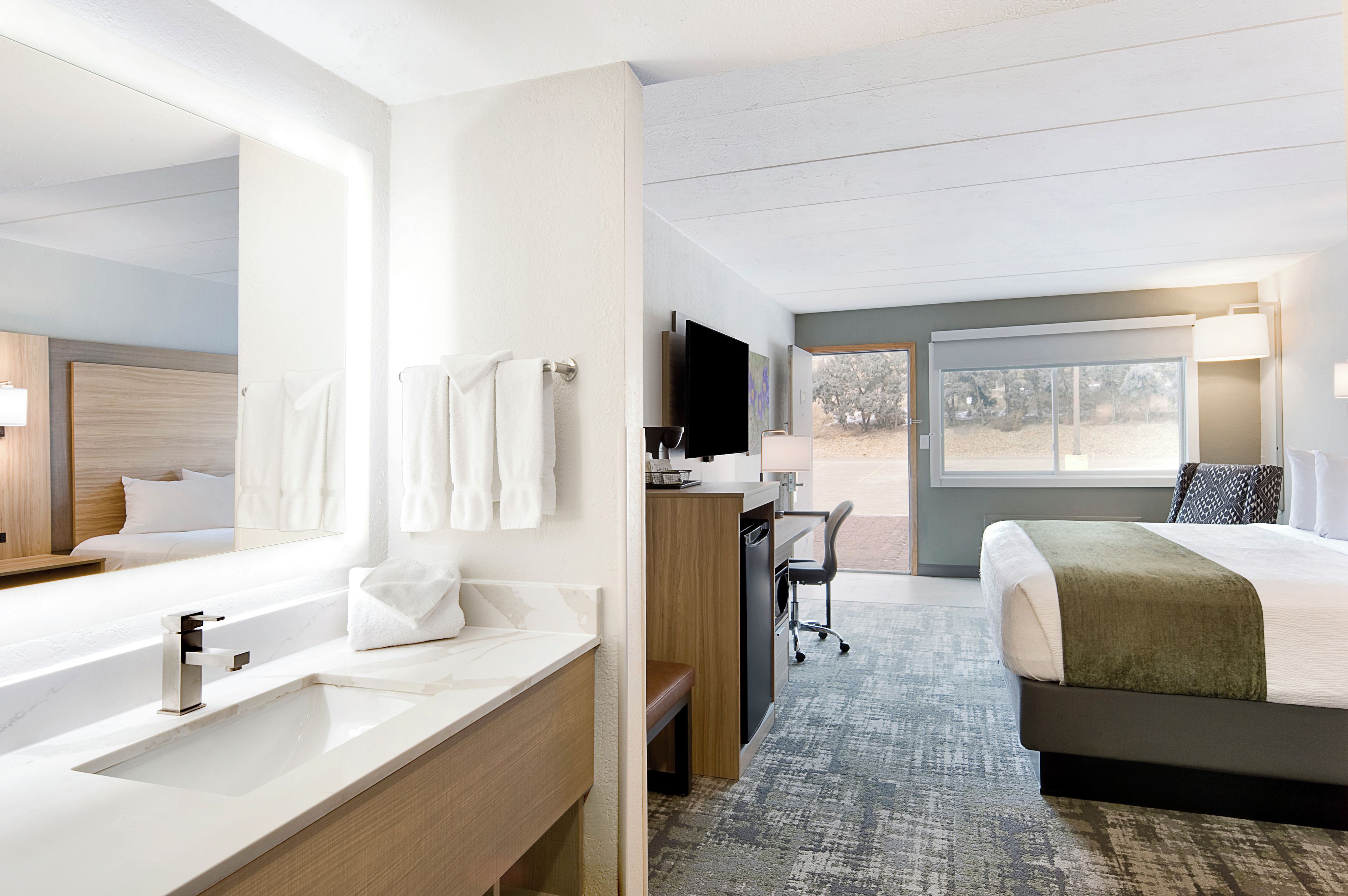 Una habitación de hotel con un espejo grande, un lavamanos, una cama, un escritorio y un televisor.