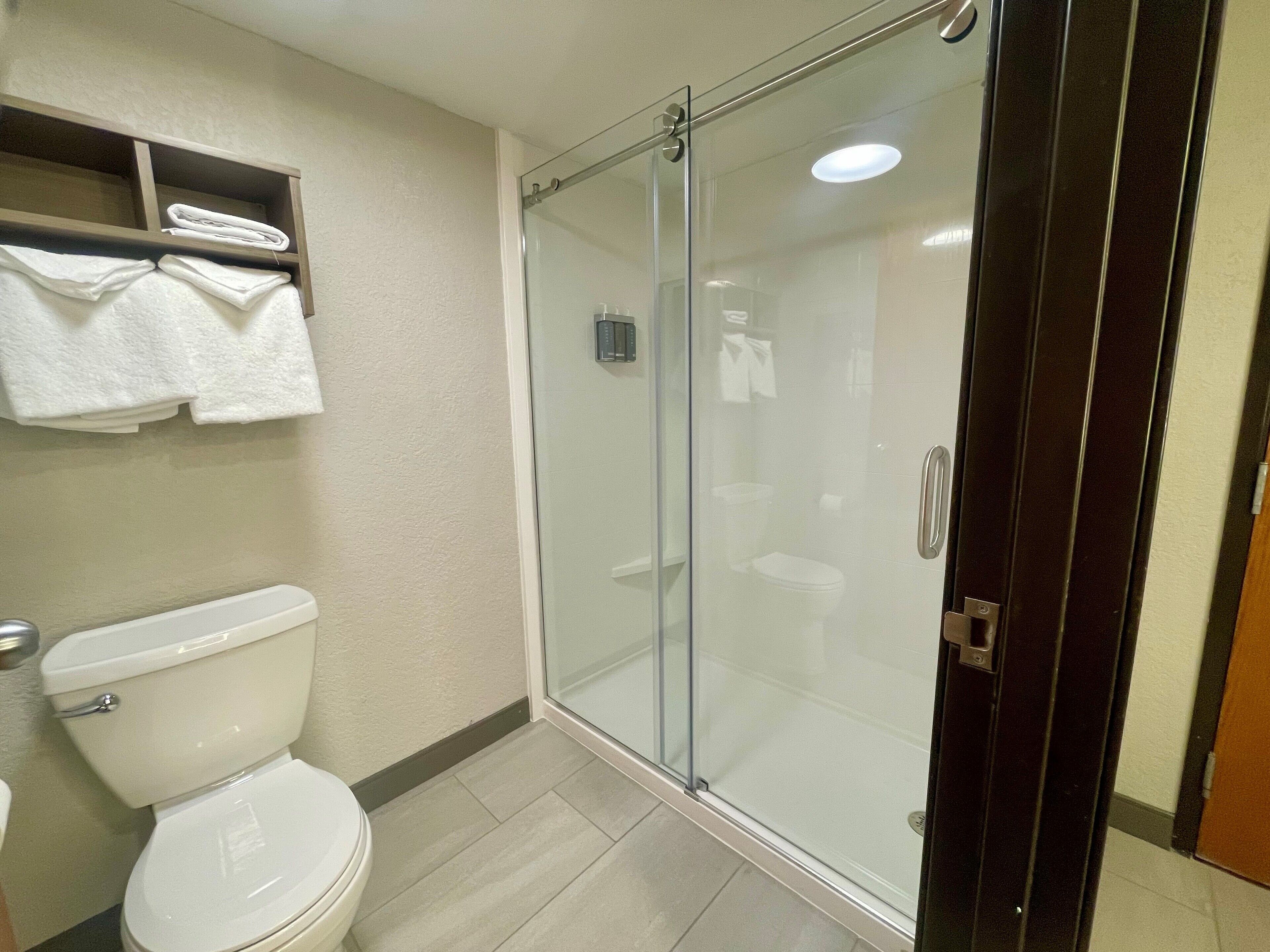 A bathroom with a toilet, a glass shower enclosure, and a shelf with folded towels.
