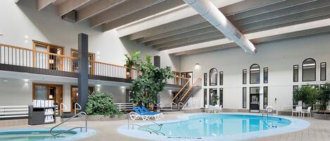An indoor swimming pool area with multiple pools, lounge chairs, and a staircase leading to an upper level.
