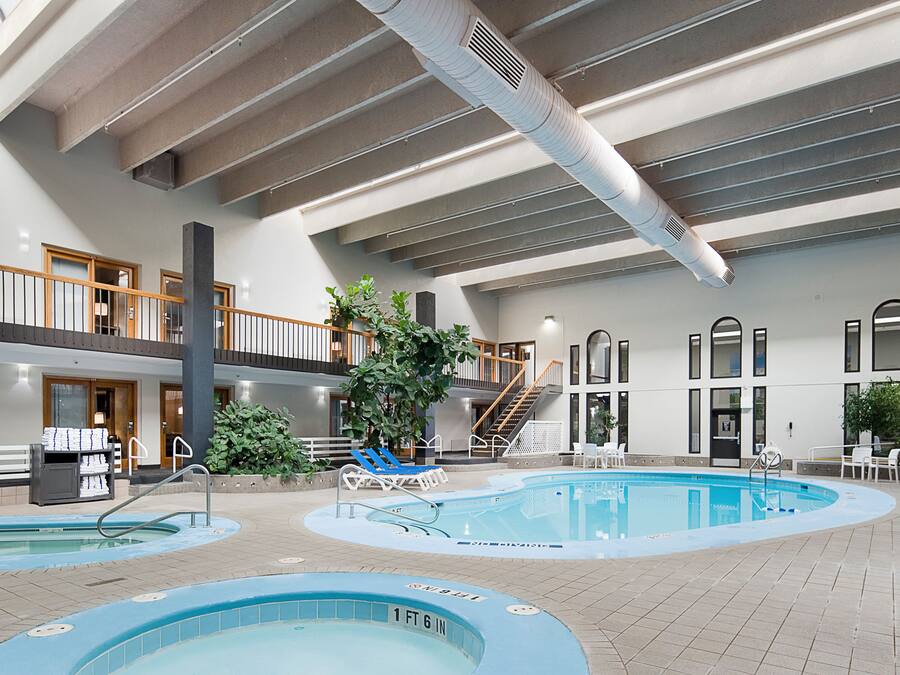 An indoor swimming pool area with multiple pools, lounge chairs, and a staircase leading to an upper level.