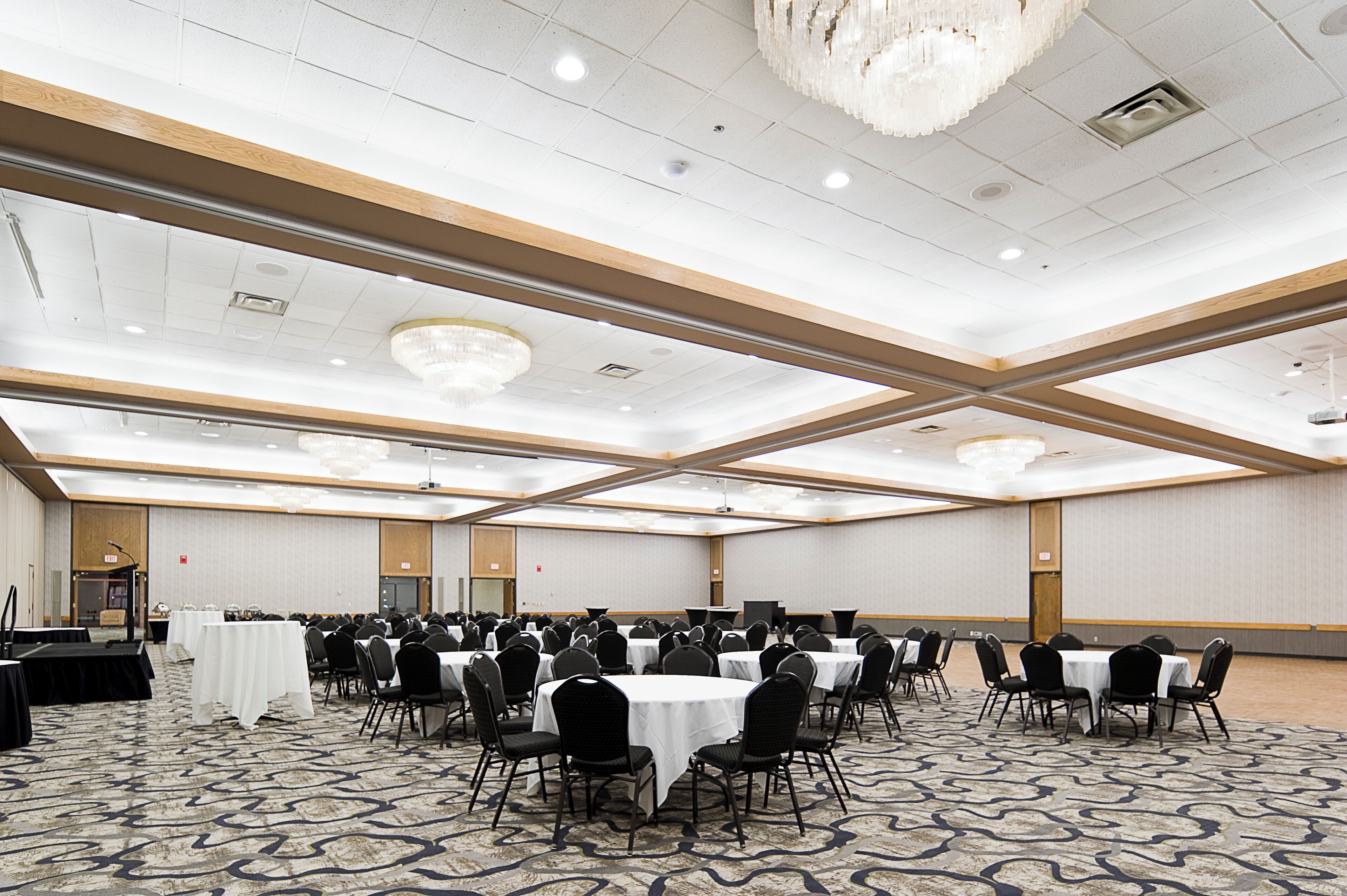 A large conference room with multiple tables and chairs, high ceilings with chandeliers, and a carpeted floor.