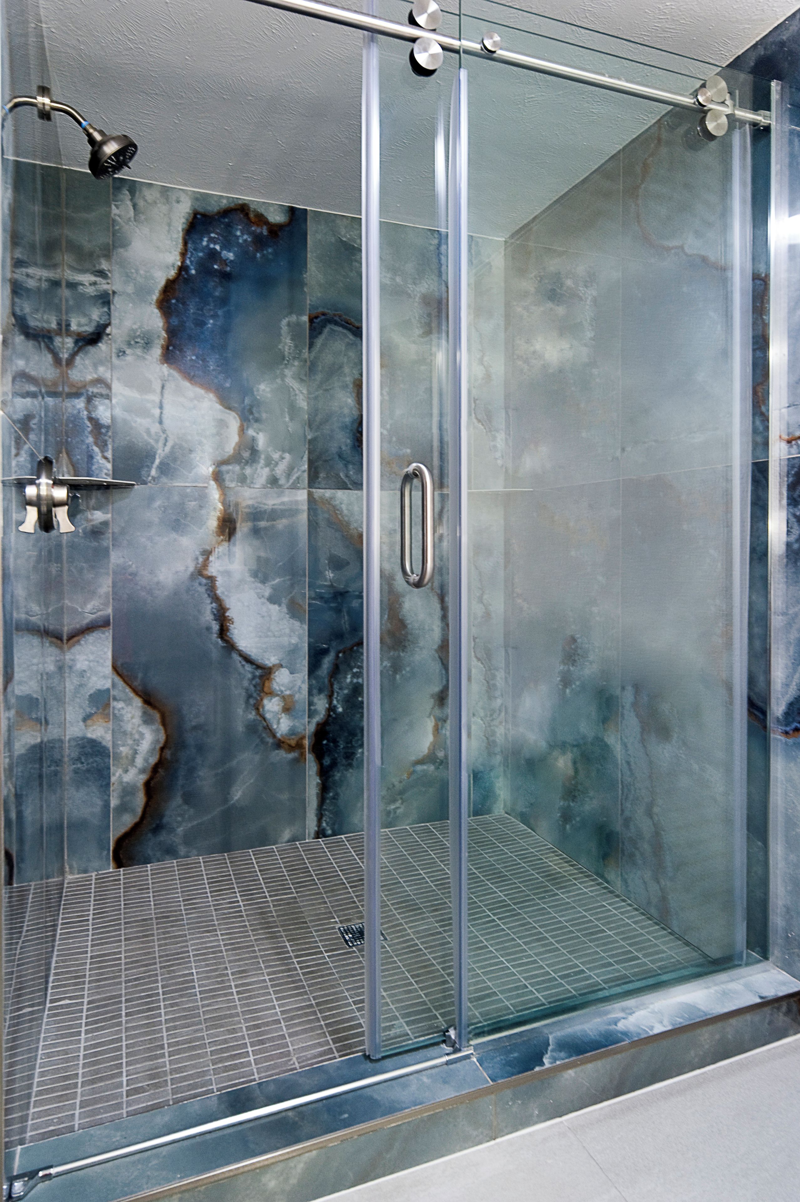 A glass-enclosed shower with a marble-like wall design.