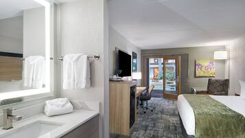 A hotel room with a large mirror, a sink, a desk with a chair, a bed, and a painting on the wall.