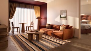 A modern hotel room with a sofa, a round coffee table, a dining table, and a chair. There is a large window with curtains, a bed with a headboard, and a wall-mounted artwork. - Seasons Of Perth (Perth)