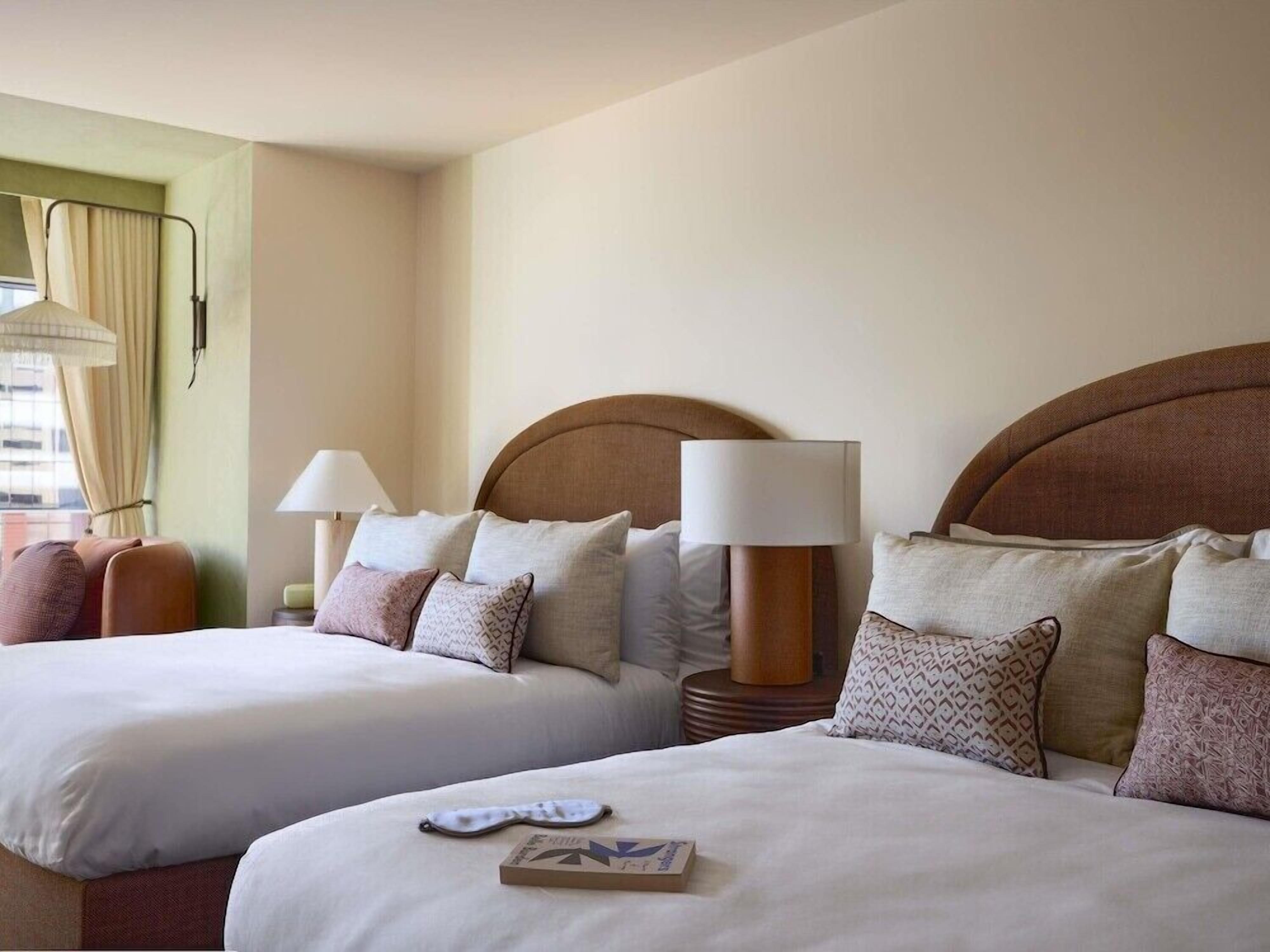A hotel room with two beds, each with a headboard, bedside lamps, and multiple pillows.