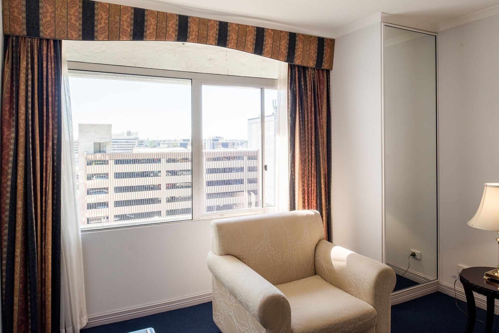 Une chambre d’hôtel avec une grande fenêtre, une chaise, une lampe et un miroir.